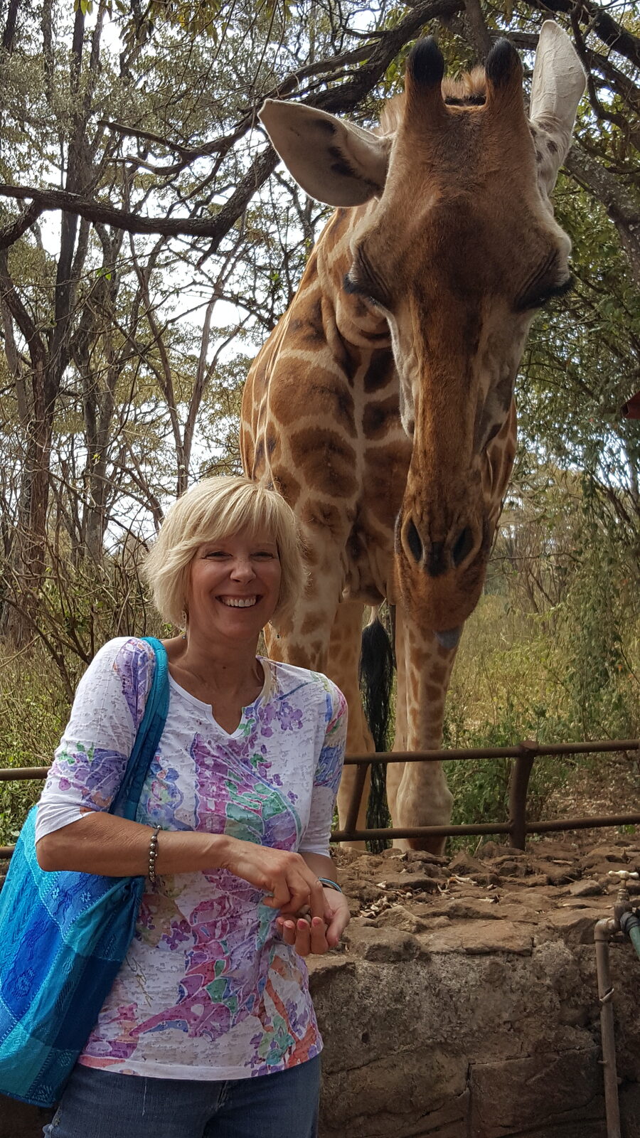 Paula Vail smiling beside a giraffe in Kenya